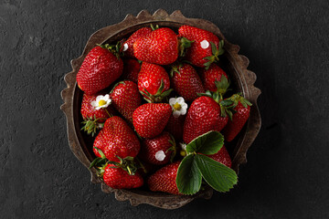 Fresh ripe organic strawberries with blossoming plant flowers in vintage metal plate on black background. top view. low key