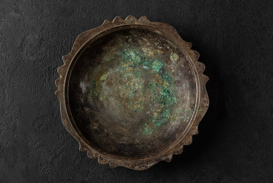 Empty vintage metal copper plate or bowl with blue rust on black stone background. low key. top view