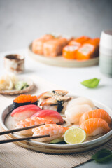 Set of sushi and maki on plate with soy sauce and chopsticks on white background. Top view with copy space