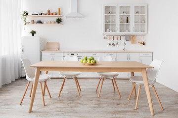 Light scandinavian kitchen interior. White furniture with various utensils, wooden table and chairs...