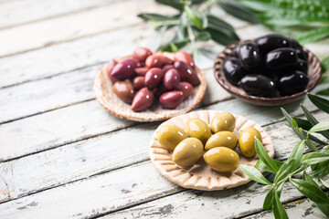 Variety of black and green olives and olive oil in bowls on white background close up