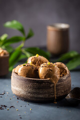 Scoops of coffee or chocolate ice cream in a bowl with green leaves on dark background
