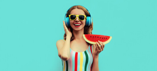 Summer portrait of cheerful happy smiling young woman in headphones listening to music with juicy slice of watermelon on a blue background