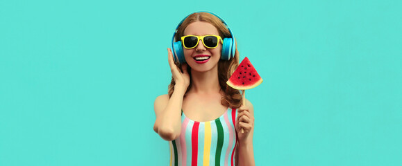 Summer portrait of cheerful happy smiling young woman in headphones listening to music with juicy slice of watermelon on a blue background
