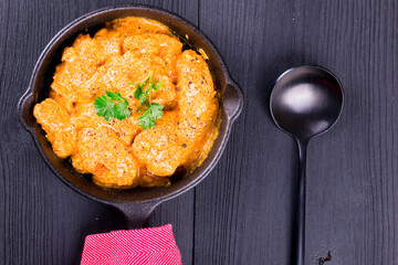 Indian Tikka Masala dish with fresh spices on a black wooden table