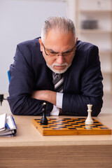 Old male employee playing chess at workplace