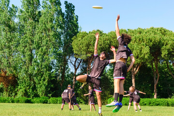 Group of young teenagers people in team wear playing a frisbee game in park oudoors. jumping man catch a frisbee to a teammate in an ultimate frisbee match. milennials friends outside in a garden - obrazy, fototapety, plakaty