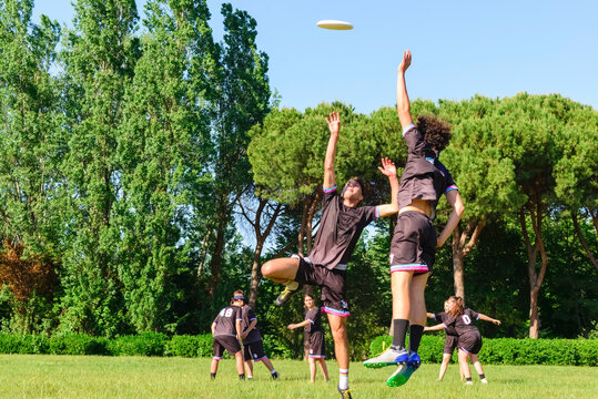 Group of young teenagers people in team wear playing a frisbee game in park oudoors. jumping man catch a frisbee to a teammate in an ultimate frisbee match. milennials friends outside in a garden