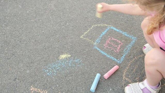 girl draws a house with chalk on the pavement on the street in summer