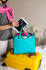 Woman hands ready travel journey putting tablet pc into handbag packing baggage at bedroom