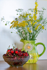 Summer still life - bowl of cherries and a bunch of wildflower s in a vase