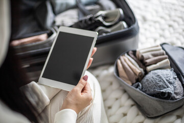 A beautiful young girl in a white casual suit sits on the bed and uses a tablet.