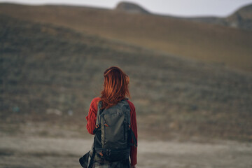 red-haired traveler with a backpack looks back on the nature in the mountains