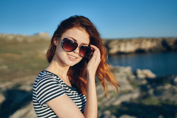beautiful red-haired woman in a t-shirt and sunglasses on nature in the mountains near the river