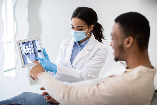 Black Female Dentist Showing Male Patient Teeth Xray Picture On Digital Tablet