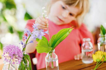 Little preschool girl making flower bouquet at home. Toddler child putting colorful garden summer...