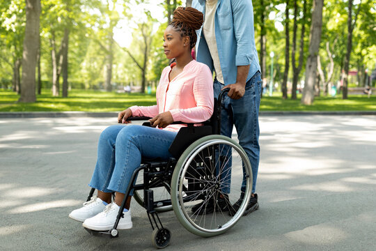Disabled black woman in wheelchair on walk with her affectionate husband outdoors, spending great time together