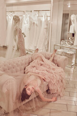 Young lady white caucasian woman with hairstyle in rose pink wedding dress posing on a pink classic sofa - 437727308