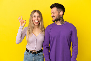 Fototapeta premium Young couple over isolated yellow background showing an ok sign with fingers