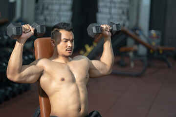 Fototapeta na wymiar Handsome adult Asian men sweating while lift up the dumbbell workout for biceps and shoulder muscle part inside of fitness gym. Bodybuilding athlete sport training for body strength and good health.