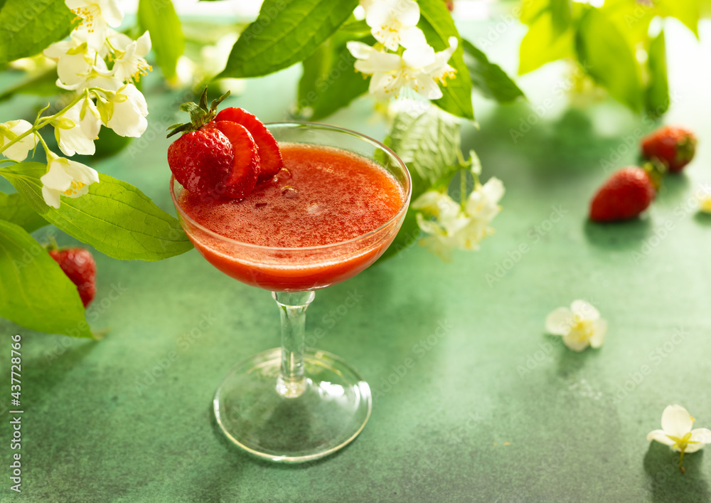 Wall mural Summer cold berry drink. Strawberry mocktail in glass decorated fresh berry and flower. Summer cocktail on green table surrounded by blooming branches