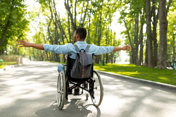 Back view of young disabled black man in wheelchair spreading his arms, feeling happy and free on...