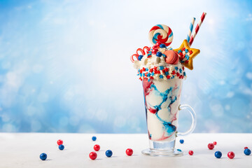 Crazy milk shake with ice cream,whipped cream, marshmallow,cookies and colored candy in glass. Sweet dessert for Fourth of July. Idea milkshake for Patriotic day.