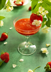 Summer cold berry drink. Strawberry mocktail in glass decorated fresh berry and flower. Summer cocktail on green table surrounded by blooming branches