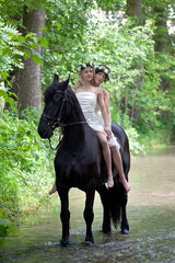 Two young woman in white dresses on a black horse