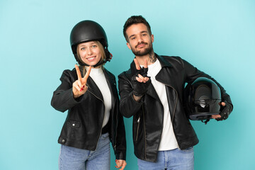 Couple with motorcycle helmet over isolated blue background smiling and showing victory sign
