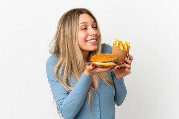 Young blonde woman holding fried chips and cheeseburger over isolated background