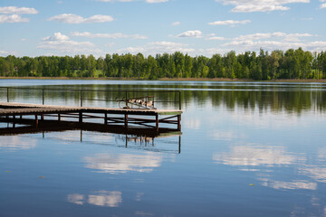 Idyllic view of the wooden pier in the lake with a forest landscape background. Wooden bridge on the lake. Long pier on the lake and blue sky in summer.