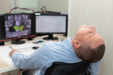 Obraz premium security guard sleeping at workplace in surveillance room. boring job concept. blurred background