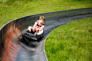 Young school kid boy having fun riding summer toboggan run sled down a hill in Hoherodskopf,...