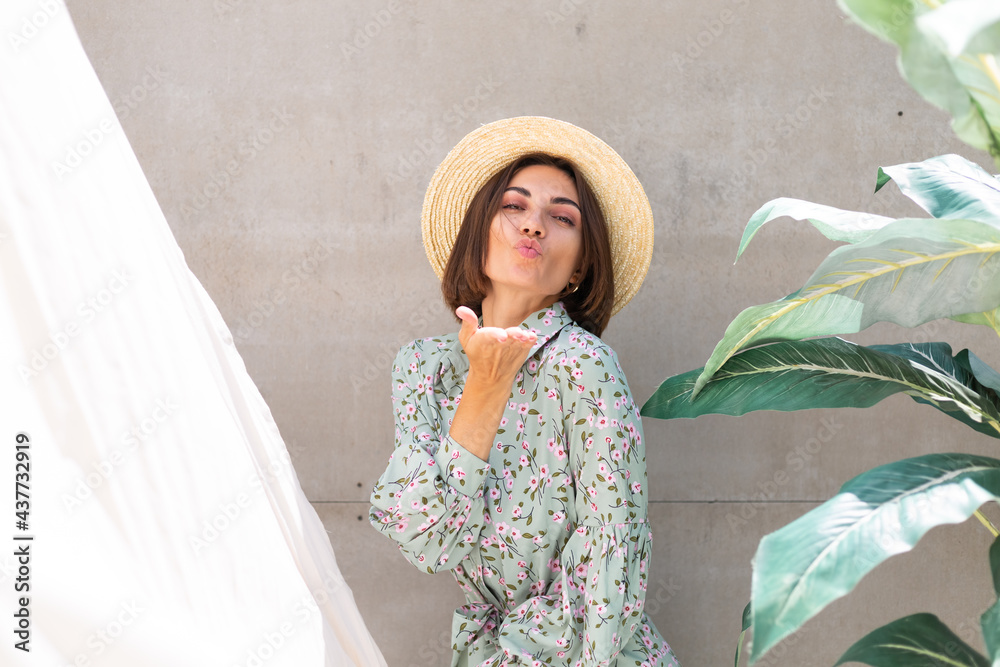 Wall mural Beautiful woman in summer dress and straw hat by palm tree and gray wall on background, playful joyful  positive excited cheerful happy