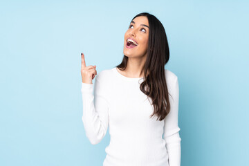 Young caucasian woman isolated on blue background pointing up and surprised