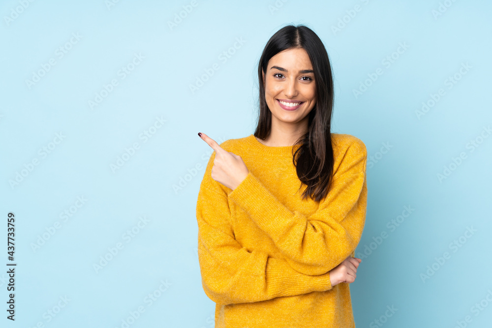 Wall mural young caucasian woman isolated on blue background pointing to the side to present a product - Wall murals