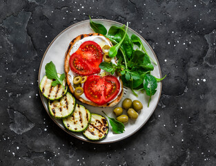Fototapeta na wymiar Sandwich with whipped ricotta, tomatoes, olives and grilled zucchini - delicious snack, tapas on a dark background, top view