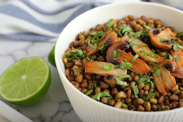 Bowl of tasty cooked lentils and mushrooms on table, closeup