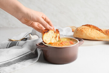 Female hand with pot of hot lentil soup and piece of bread on white background