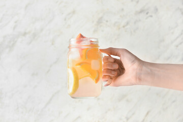 Woman holding mason jar of tasty cold lemonade on light background