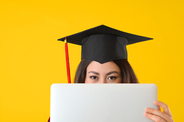 Female graduating student with laptop on color background