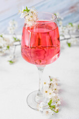 Glass with tasty drink and blooming branches on light background
