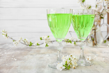 Glasses with tasty drink and blooming branches on grunge background