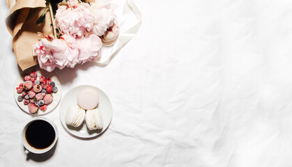 coffee, peonies and macaroons on white bed linen. Breakfast in bed. Scandinavian style. Flat lay, top view 