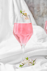 Glass with tasty drink and blooming branches on light background