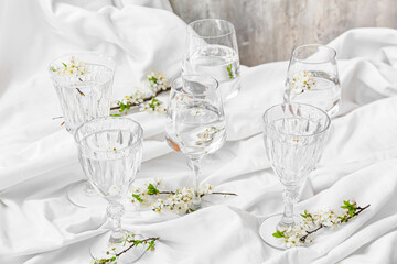 Glasses with water and blooming branches on light background