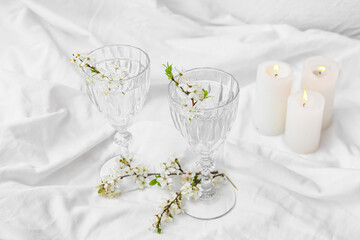 Glasses with water and blooming branches on light background