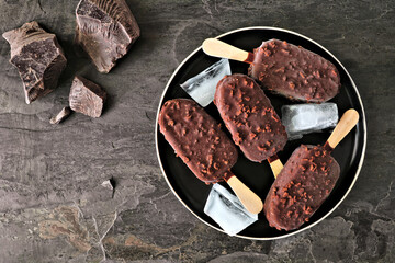 Plate of chocolate dipped ice cream bars with nuts. Overhead view over a dark slate background.