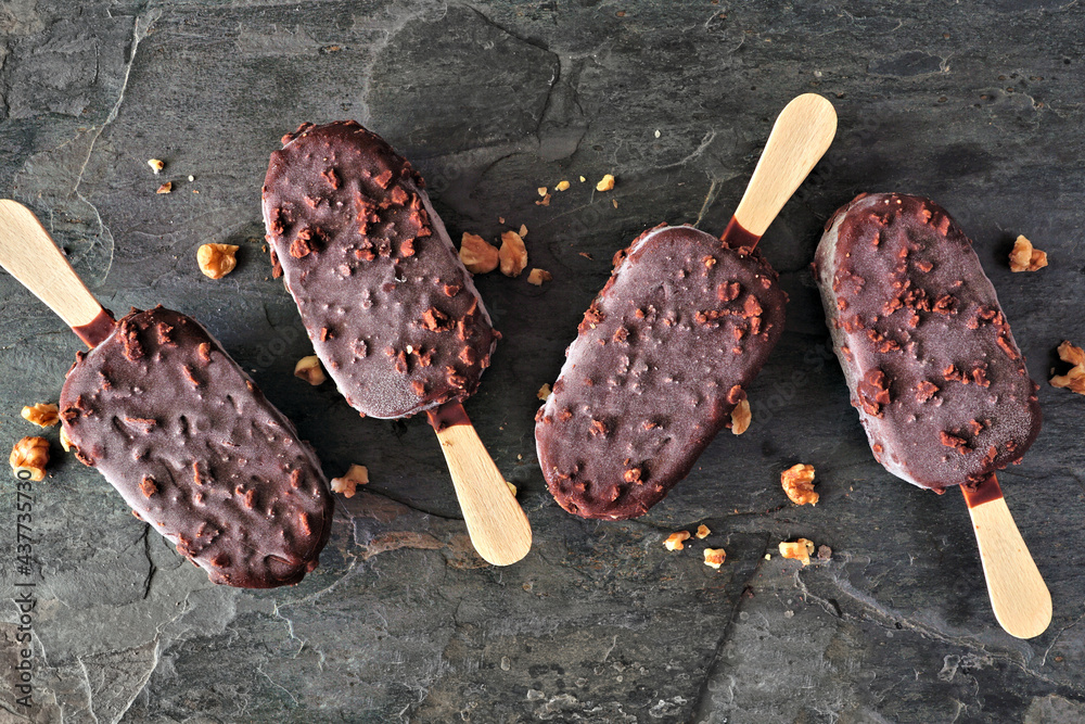 Poster chocolate dipped ice cream bars with nuts. overhead view scattered on dark slate background.